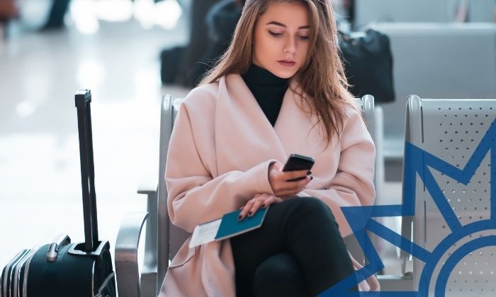 Frau mit Ticket, Koffer und Smartphone im Wartebereich eines Flughafens.