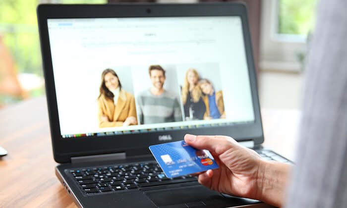 Ein Mann beim Online-Shopping mit Kreditkarte in der Hand vor dem Laptop.