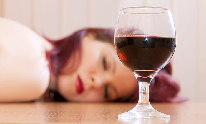 Frau liegt schlafend neben Rotweinglas.