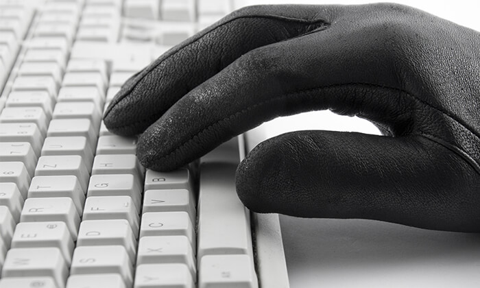 Hand mit schwarzem Handschuh an PC-Tastatur.