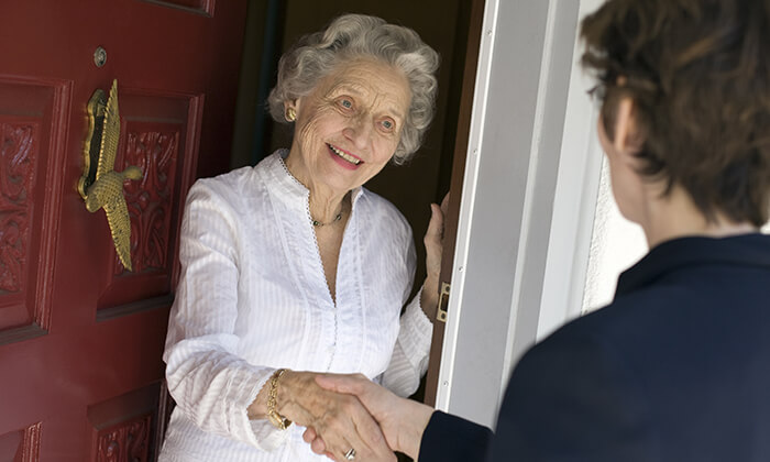 Seniorin reicht Besucher an der Haustür die Hand.