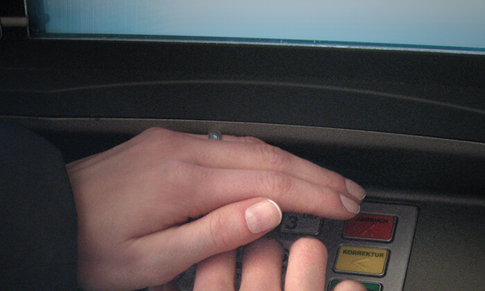 Hand verdeckt das Tastenfeld eines Geldautomaten bei Eingabe der PIN.