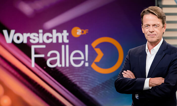 Rudi Cerne vor "Vorsicht, Falle!" Logo im TV Studio