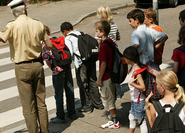 Polizist zeigt Schülern sichere Überquerung eines Zebrasteifens.