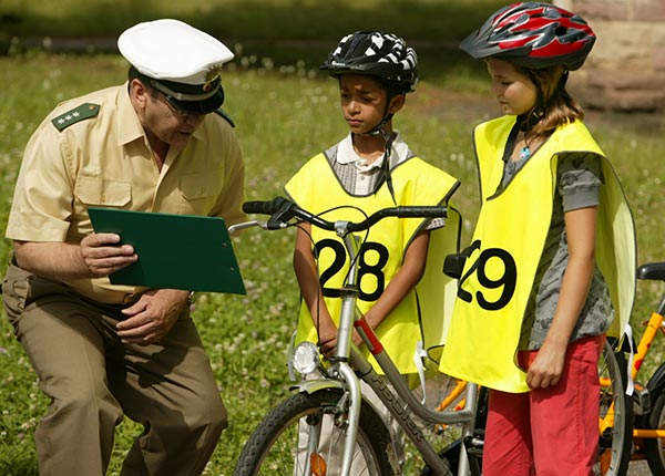 Verkehrspolizist zeigt zwewi Kindern, wie sie sicher Fahrradfahren.