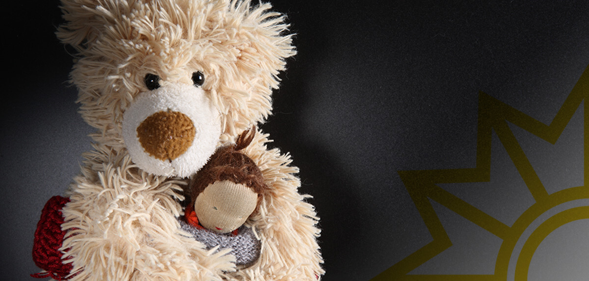 Vertrauen. Teddybär hält Puppe schützend im Arm
