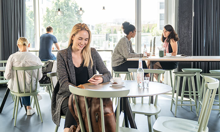 Junge Frau sitzt auf ihr Smartphone blickend in einem Café