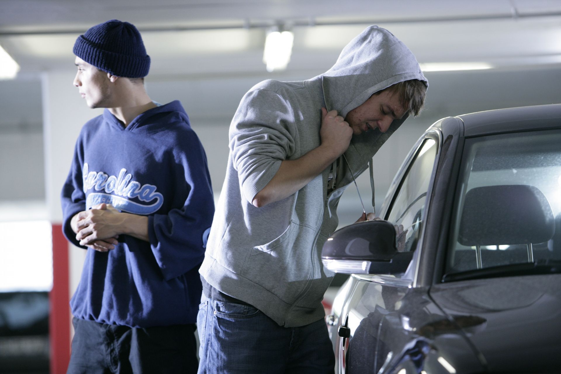 Ein junger Mann knackt ein Auto auf. Ein zweiter hält Wache.