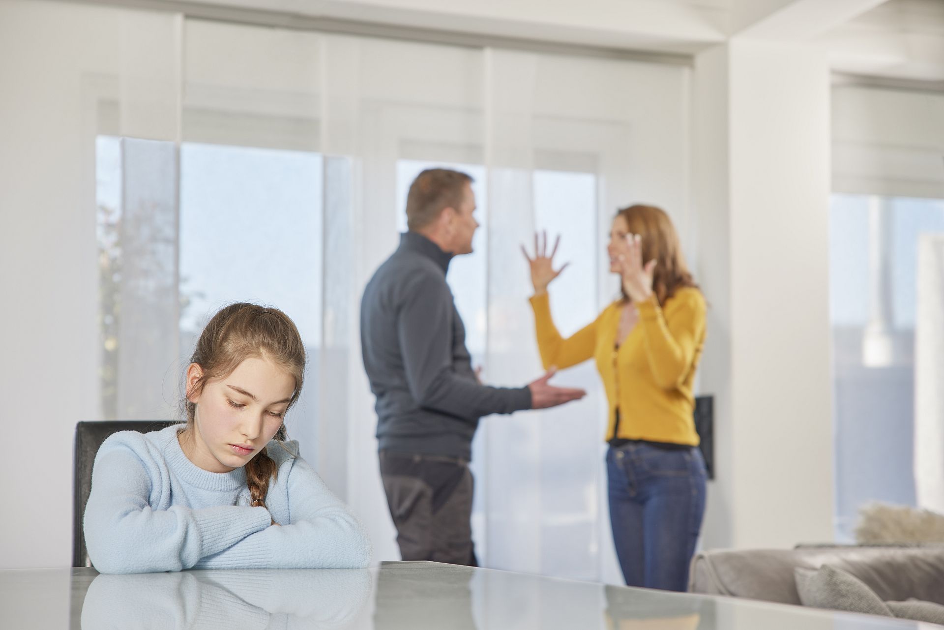 Eltern streiten und die Tochter sitzt währenddessen traurig am Tisch.