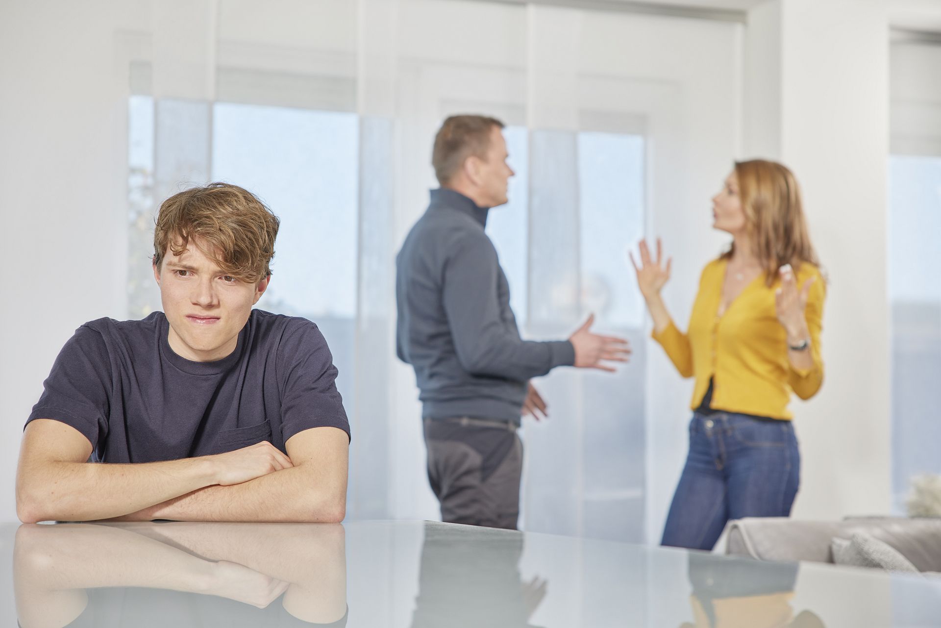 Eltern streiten und Sohn sitzt wütend am Tisch.