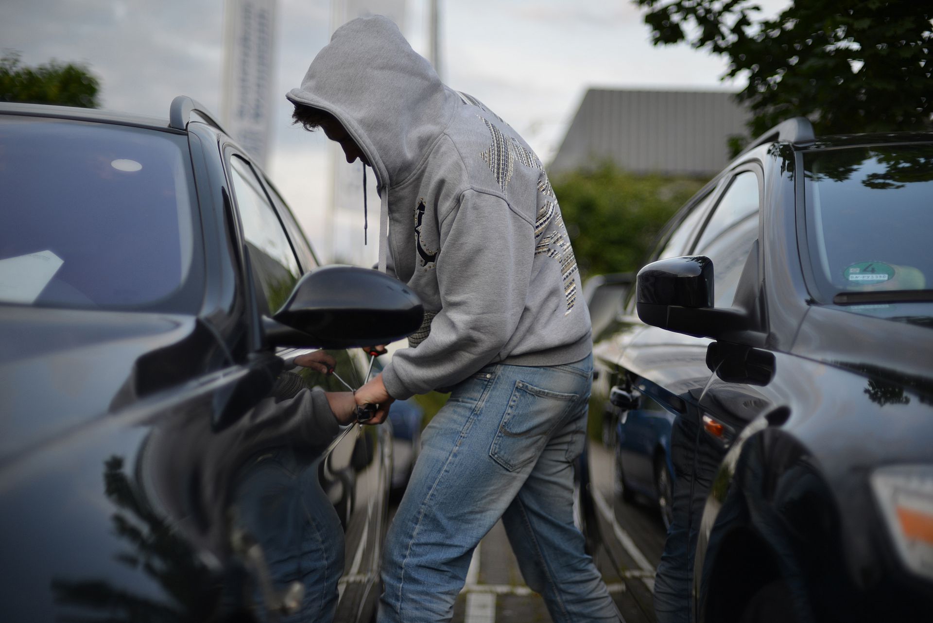 Ein Mann hebelt mit einem Schraubendreher eine Autotür auf.