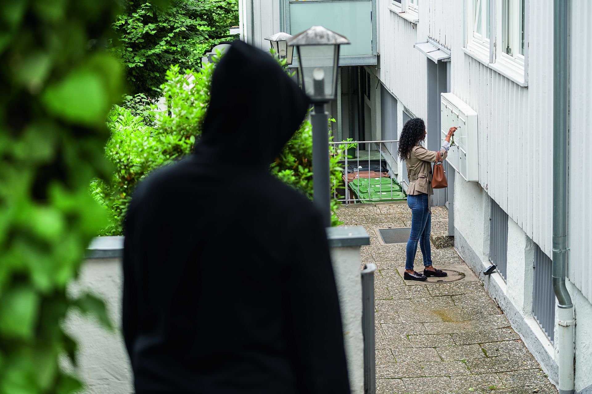 Ein Mann beobachtet eine Frau, die gerade ihren Briefkasten leert.