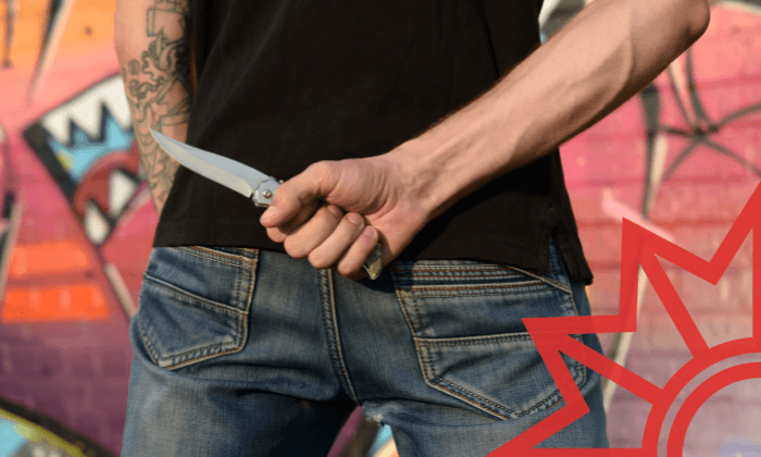 Mann hält ein Messer mit feststehender Klinge hinter seinem Rücken versteckt.