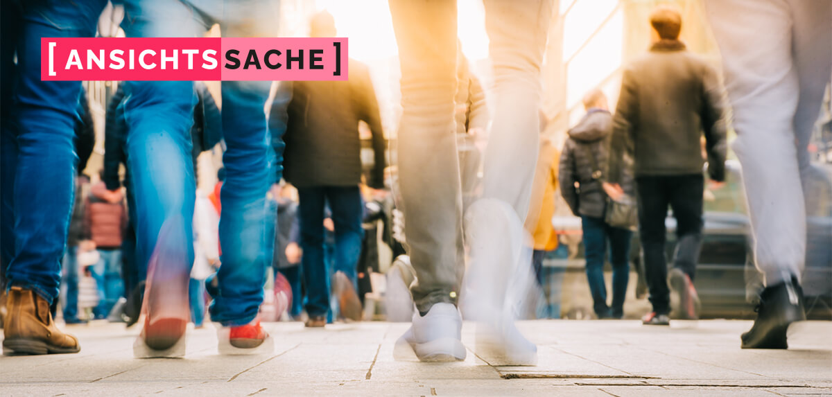 Straßenszene mit mehreren Menschen, die zu Fuß unterwegs sind, teils in Bewegung verschwommen aufgenommen. Links oben der Schriftzug "[Ansichtssache]".