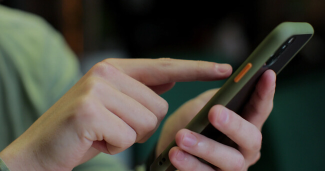 Nahaufnahme einer Person, die mit dem Finger auf den Bildschirm eines Smartphones tippt. Das Smartphone befindet sich in einer grün-schwarzen Hülle.