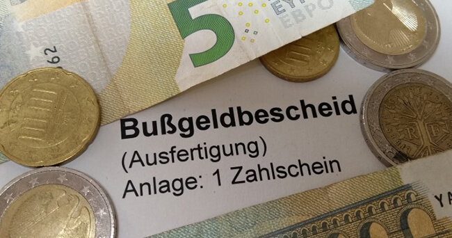 Mehrere Euro-Geldscheine und Münzen liegen auf einem Dokument mit der Aufschrift „Bußgeldbescheid (Ausfertigung) Anlage: 1 Zahlschein“.