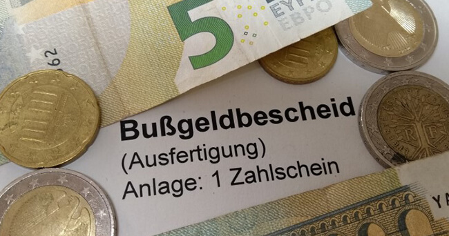 Mehrere Euro-Münzen und Geldscheine liegen auf einem Schriftstück mit der Aufschrift „Bußgeldbescheid (Ausfertigung) Anlage: 1 Zahlschein“.