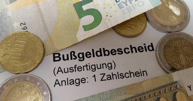 Mehrere Euro-Münzen und -Scheine liegen auf einem Schriftstück mit der Aufschrift „Bußgeldbescheid (Ausfertigung) Anlage: 1 Zahlschein“.