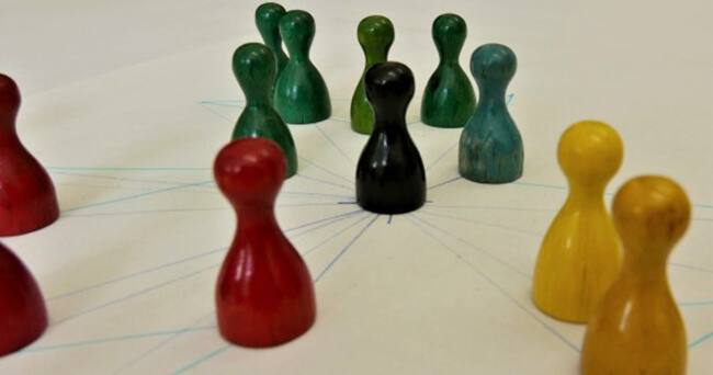 Verschiedenfarbige Spielfiguren stehen auf einem Papierraster in Gruppen um eine zentrale Figur, symbolisch für Vernetzung und Bürgerengagement im Stadtteil.