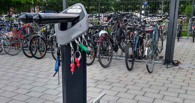 An einer Fahrrad-Servicestation mit Luftpumpe und Werkzeug hängen mehrere Schlüssel, im Hintergrund sind zahlreiche abgestellte Fahrräder zu sehen.