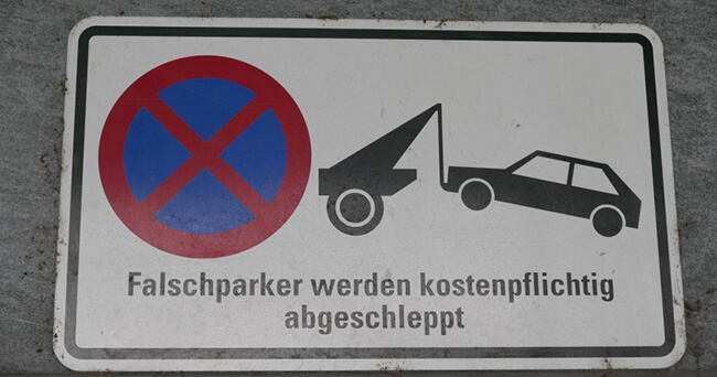 Rechteckiges Schild mit Piktogramm eines Autos, das von einem Abschleppfahrzeug gezogen wird, und der Aufschrift „Falschparker werden kostenpflichtig abgeschleppt“.
