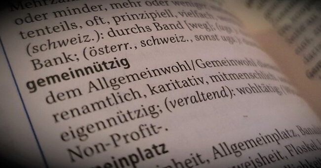 Ein aufgeschlagenes Wörterbuch zeigt den fett gedruckten Begriff „gemeinnützig“ mit Definitionen wie „dem Allgemeinwohl dienend“ und „karitativ“.