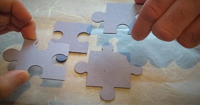 Zwei Hände setzen mehrere Puzzleteile zu einem Ganzen zusammen.