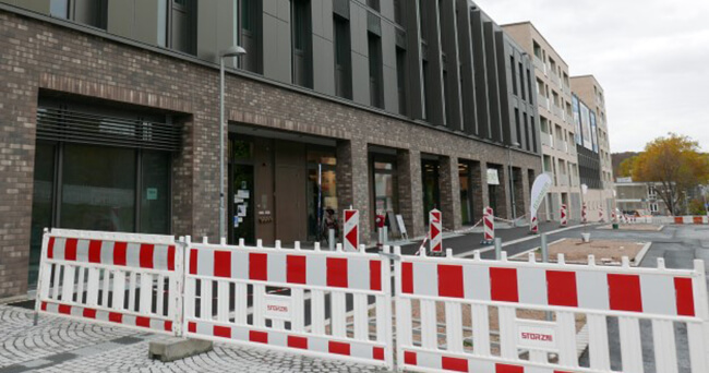 Eine abgesperrte Baustelle im öffentlichen Raum, im Hintergrund moderne Gebäude.