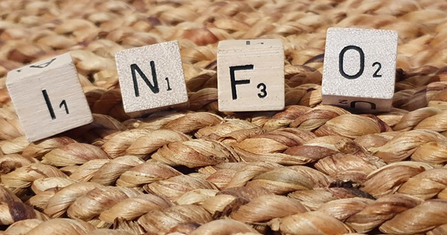 Nahaufnahme von vier Scrabble-Buchstaben, die das Wort „INFO“ bilden, auf einer geflochtenen Unterlage liegend.