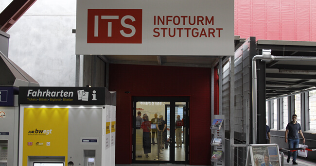 Blick auf den Eingang des Info-Zentrums am Bahnhof Stuttgart mit Fahrkartenautomat links und Personen im Hintergrund.