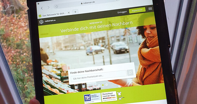 Tablet, auf dem die Startseite einer Nachbarschaftshilfe-Website angezeigt wird, mit Suchfeld zur Eingabe der Postleitzahl und dem Slogan „Verbinde dich mit deinen Nachbarn“.