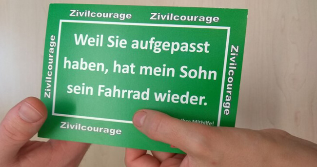 Zwei Hände halten eine grüne Dankeskarte mit dem Text: „Weil Sie aufgepasst haben, hat mein Sohn sein Fahrrad wieder.“ Die Karte trägt mehrfach den Schriftzug „Zivilcourage“.