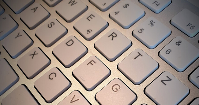 Ausschnitt einer Computertastatur in silberner Farbe, schräg fotografiert, mit deutlich erkennbaren Buchstaben- und Sonderzeichentasten.