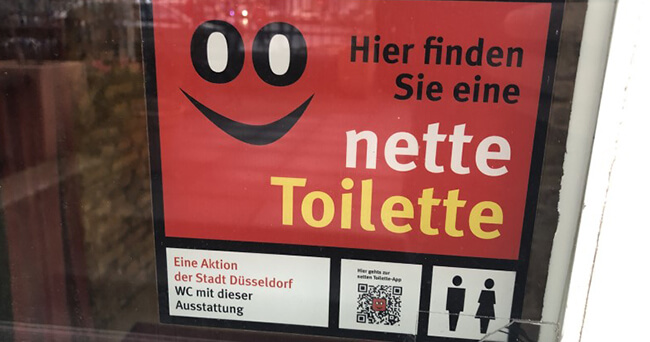 Eingang eines Unternehmens mit Aufkleber der Aktion „Die Nette Toilette“, der darauf hinweist, dass hier die Toiletten kostenlos für die Öffentlichkeit zugänglich sind.