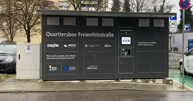 Schwarze Quartiersbox an der Freienfelsstraße mit Bedienfeld und Beschriftung zur Abholung und Aufbewahrung von Gegenständen, aufgenommen in einer städtischen Umgebung.
