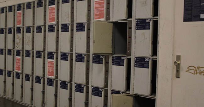 Mehrere graue Schließfächer in einer Reihe, teils mit offenen Türen, in einem öffentlichen Bereich.