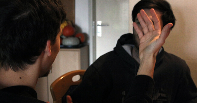 Zwei Personen sitzen sich gegenüber, eine Person hebt die Hand in einer sprechähnlichen Geste, der Hintergrund ist unscharf.