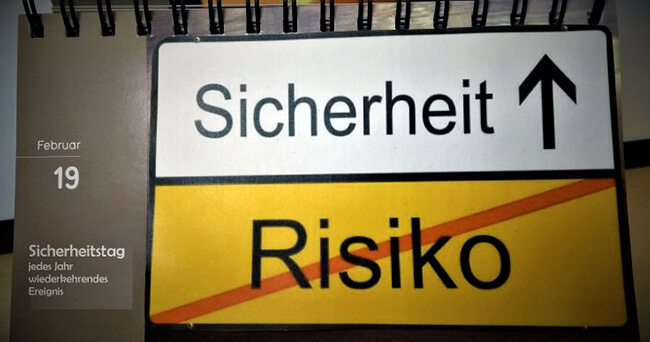 Auf einem Tischkalender ist ein Verkehrsschild mit der Aufschrift „Sicherheit“ und durchgestrichenem „Risiko“ abgebildet. Links steht das Datum 19. Februar mit dem Hinweis „Sicherheitstag – jedes Jahr wiederkehrendes Ereignis“.