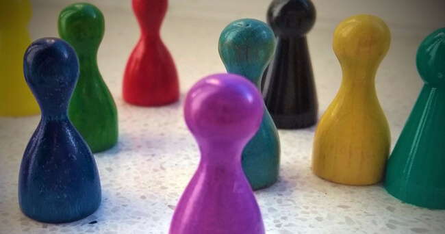 Mehrere unterschiedlich farbige Spielfiguren stehen im Kreis auf hellem Untergrund und symbolisieren soziale Vielfalt und Integration.