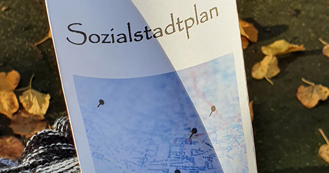 Nahaufnahme eines Faltplans mit der Aufschrift „Sozialstadtplan“ vor herbstlich gefärbten Blättern.