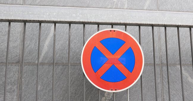 Rundes Verkehrsschild „Absolutes Halteverbot“ an einem Metallgitter, aufgenommen vor einer grauen Steinwand.