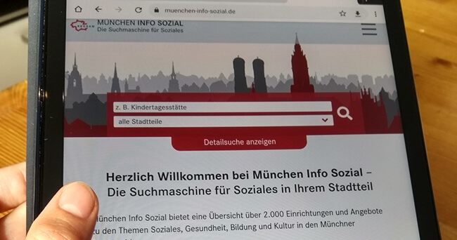 Auf einem Tablet ist die Startseite einer städtischen Suchmaschine für soziale Einrichtungen geöffnet. Zu sehen ist eine Eingabemaske mit der Auswahl von Stadtteilen und ein Begrüßungstext mit Suchoptionen.