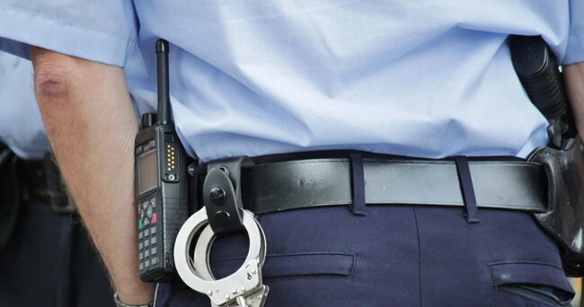 Ein Polizist in Uniform mit Funkgerät und Handschellen am Gürtel steht mit dem Rücken zur Kamera, bereit für den Einsatz.