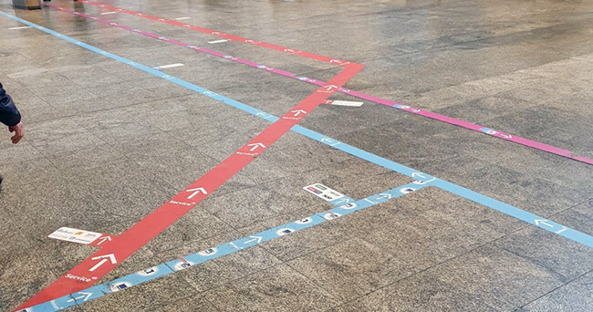 Bodenmarkierungen mit farbigen Linien und Richtungspfeilen in einer Halle zur besseren Orientierung für Fußgängerinnen und Fußgänger