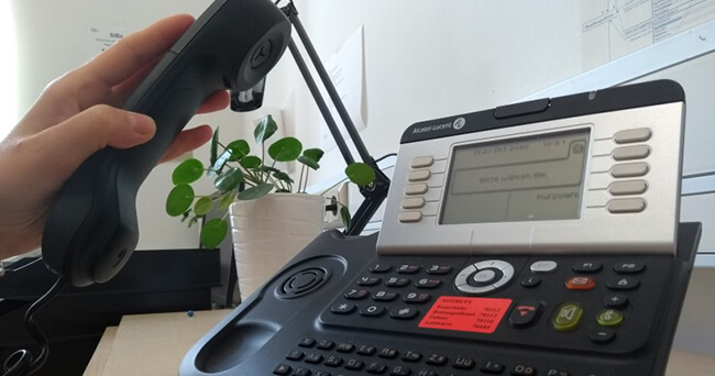 Hand hält den Hörer eines Bürotelefons, Symbol für eine zentrale Anlaufstelle zu Sicherheitsfragen in der Stadtverwaltung.