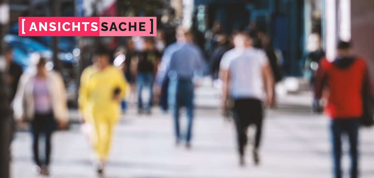 Straßenszene mit mehreren unscharf aufgenommenen Fußgängerinnen und Fußgängern in einer belebten Einkaufsstraße. Links oben der Schriftzug "[Ansichtssache]".