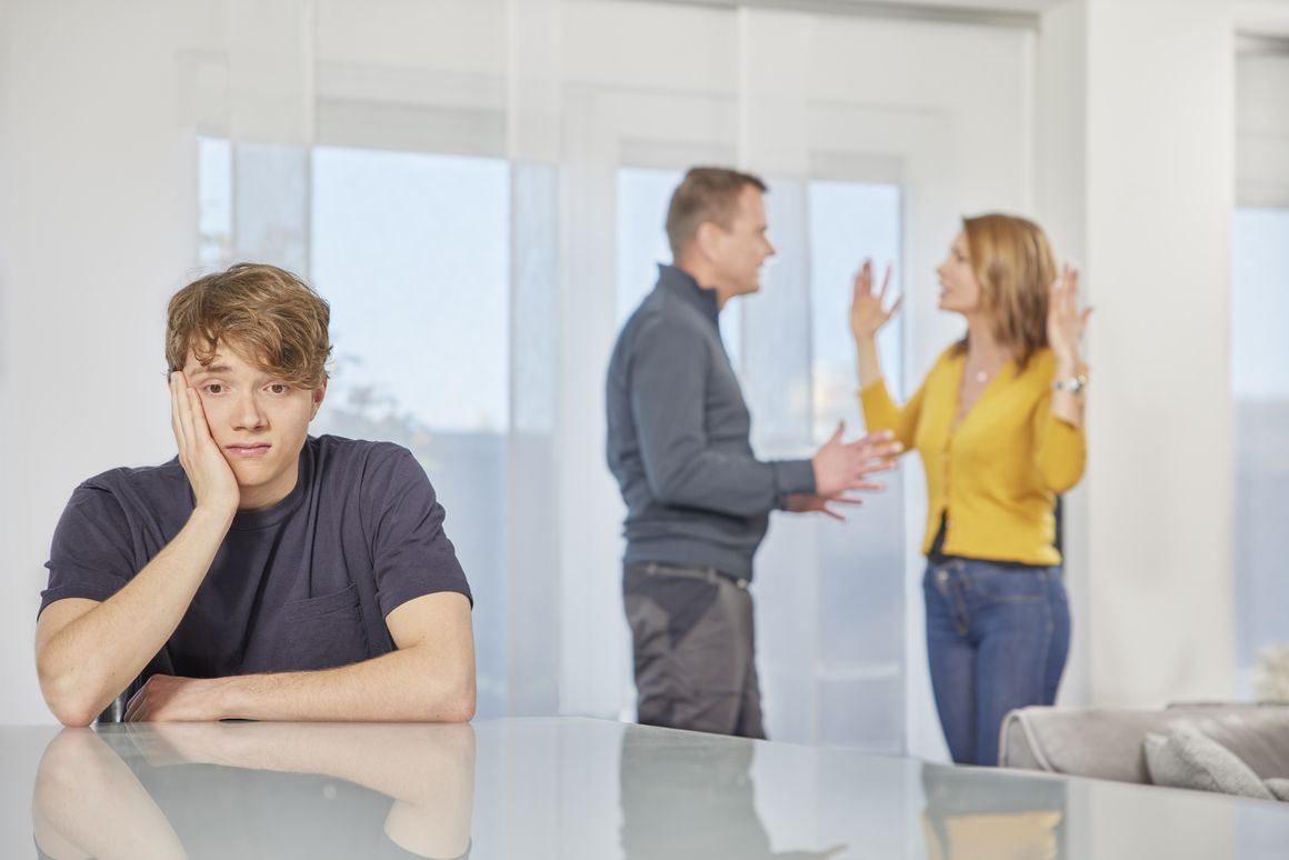 Eltern streiten und Sohn sitzt mit leerem Blick am Tisch.